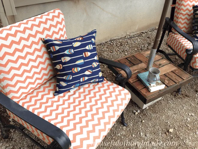 patio chair with orange and white cushion and blue print pillow with diy umbrella stand with a wood top side table 