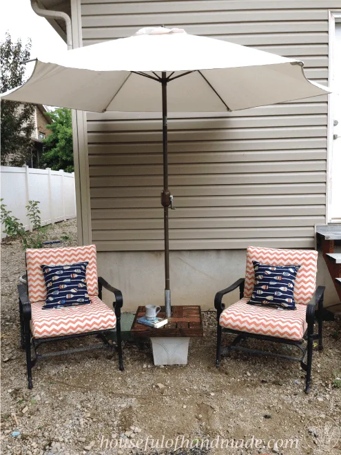 diy umbrella stand side table shown on patio with two patio chairs and a white umbrella