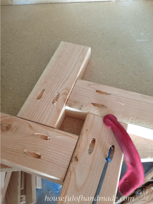 four pieces of cut wood shown with clamp to hold base of DIY patio stand