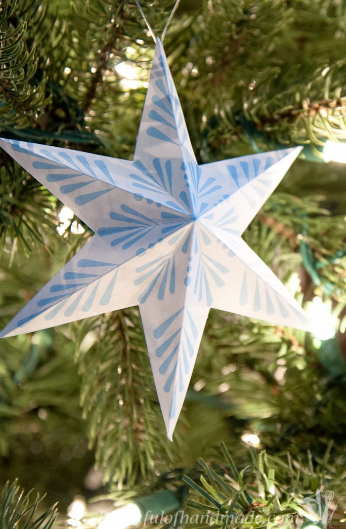 blue and white diy paper snowflake ornament hanging in a tree