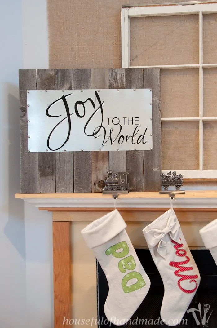 reclaimed wood and steel Christmas sign shown on mantel with stocking holders and two stockings