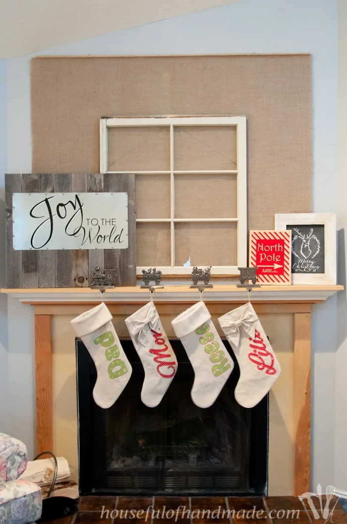 reclaimed wood and steel Christmas sign shown on fireplace mantel with four hanging stockings.