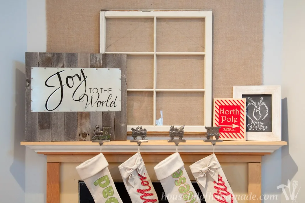 DIY reclaimed wood and steel Christmas sign displayed on fireplace mantel with old window and stockings. 