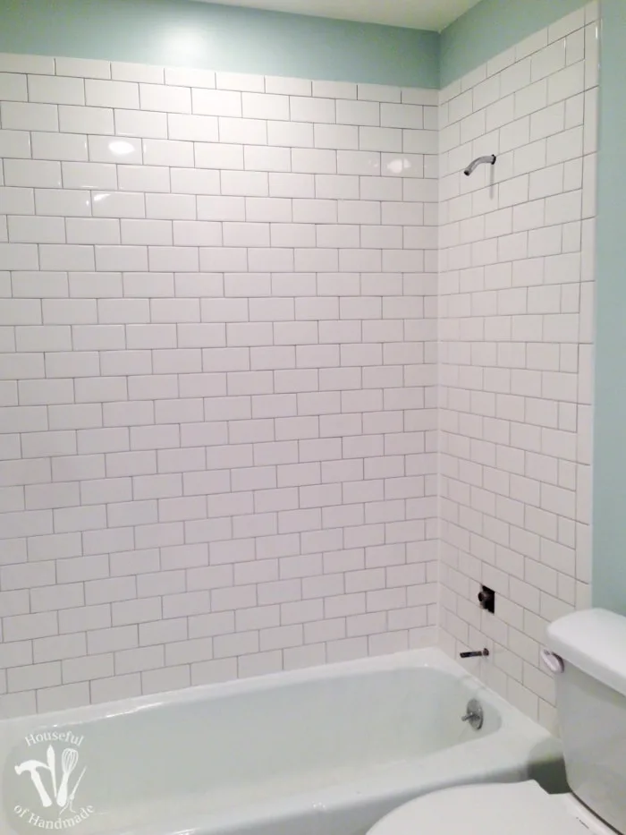 Bath tub surround tiled with 3x6 individual white ceramic subway tiles and grouted with a medium gray grout.