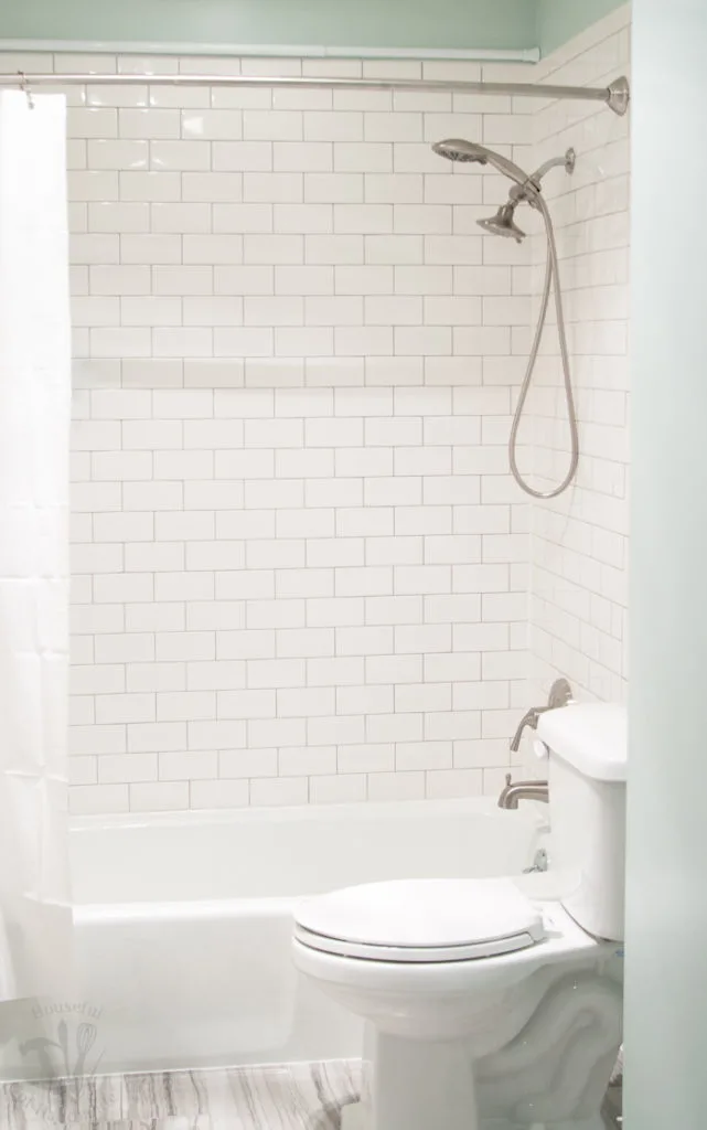 Tub and shower area tiled with classic white subway tiles and a white shower curtain. 