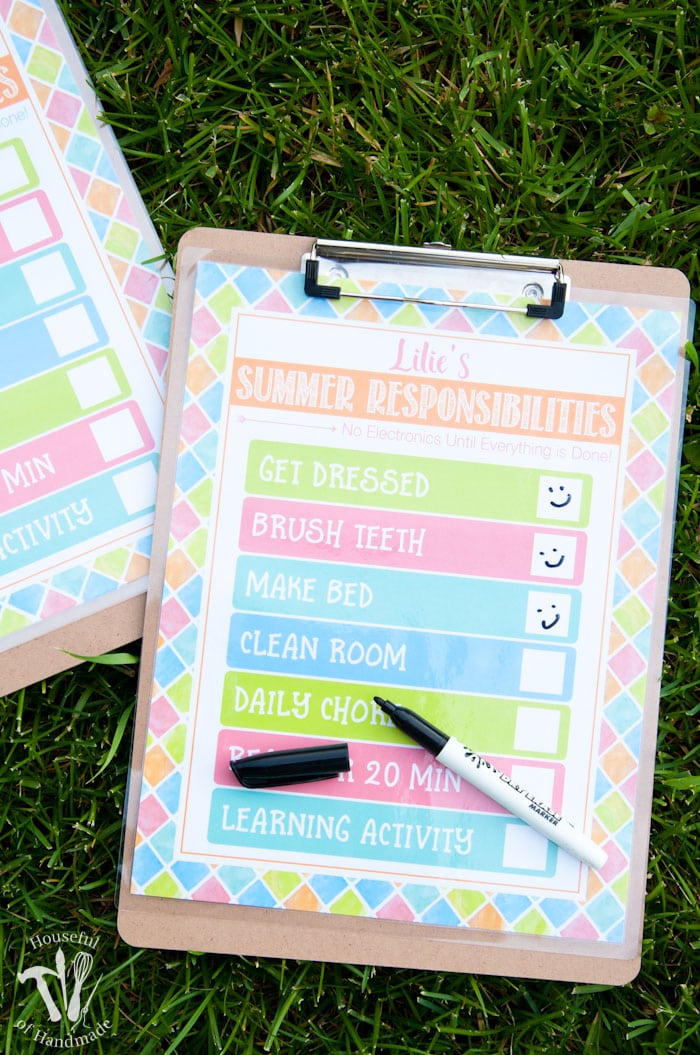 two clipboards shown on grass with free printable summer chore chart attached and an uncapped pen on top of printable