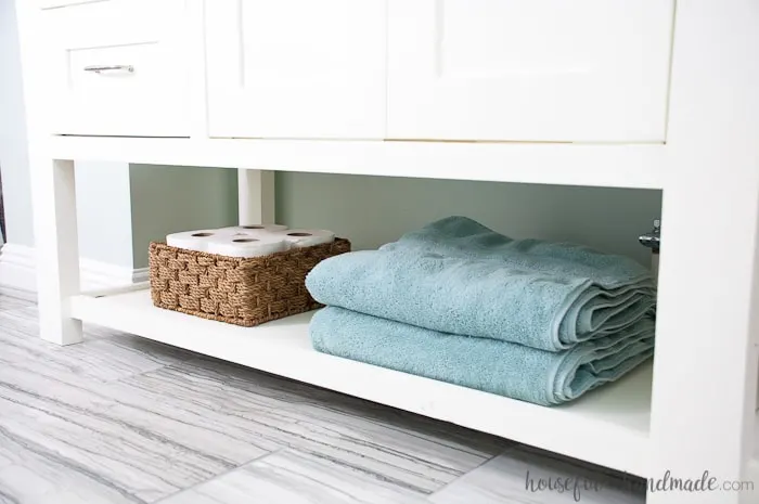 Large open shelf on the bottom of a DIY vanity with towels and toilet paper on it. 