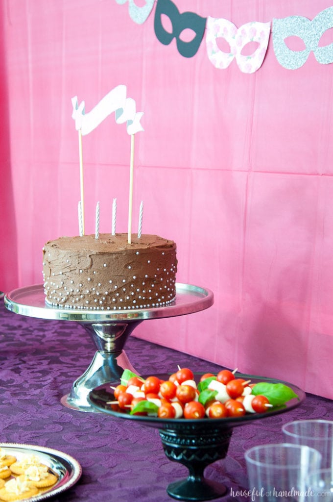 chocolate cake on a stand next to caprese skewers for a masquerade ball themed birthday