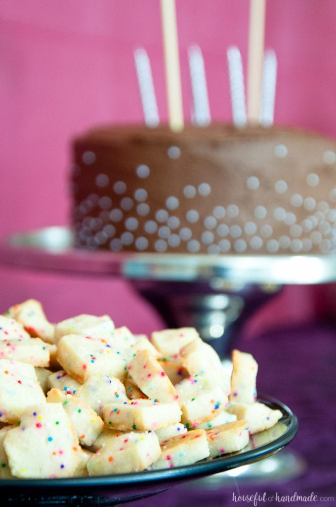 a plate of cookies with sprinkles  on a table with a cake behind at a masquerade ball themed birthday