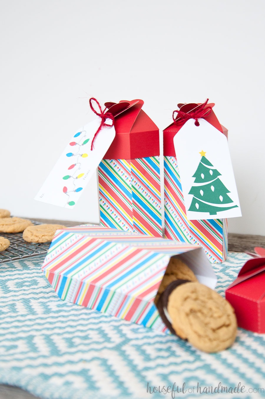 Three colorful tall Christmas cookie boxes, one tipped over, filled with a stack of cookies.