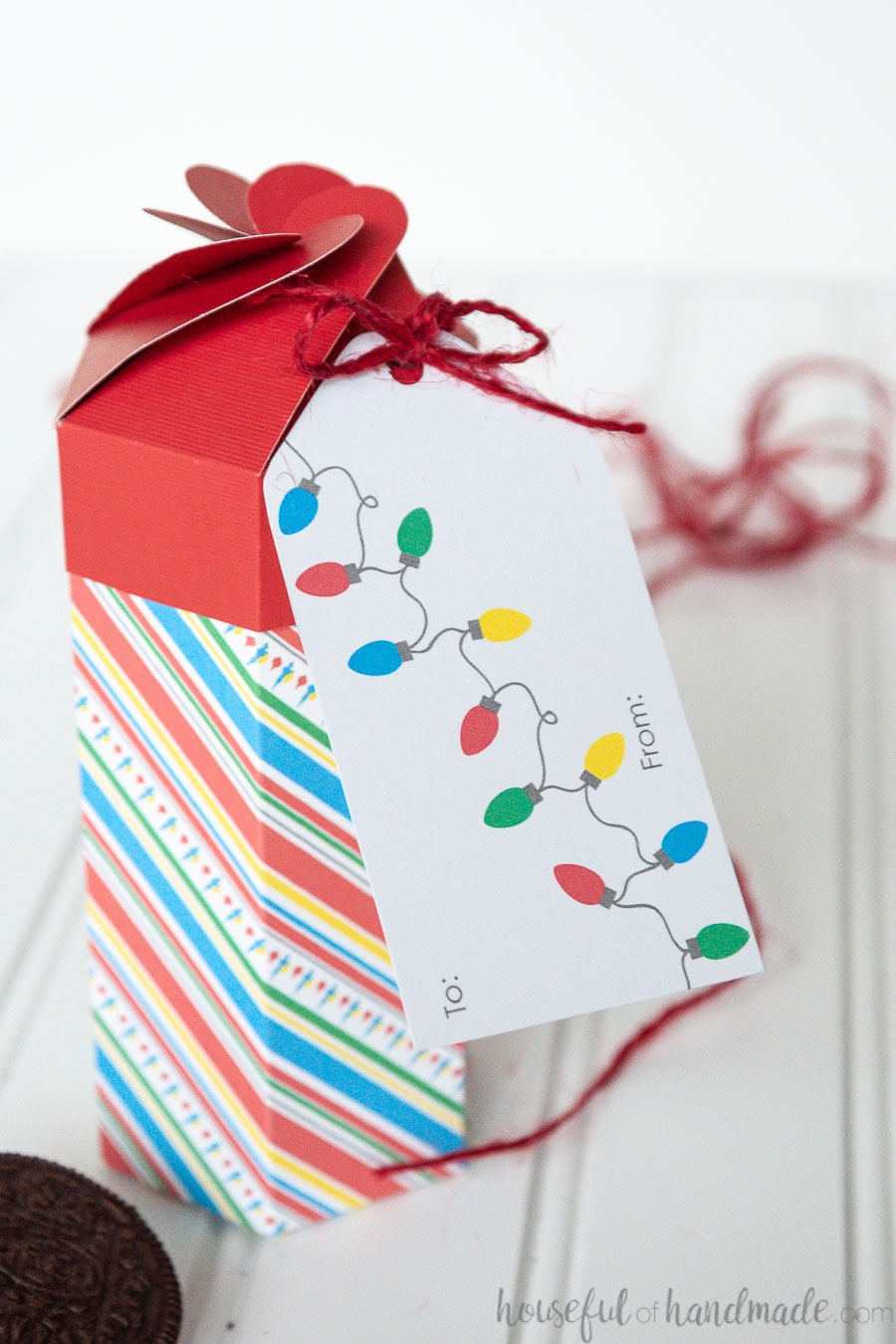 A Christmas gift tag attached to the lid of the tall cookie box with red twine. 