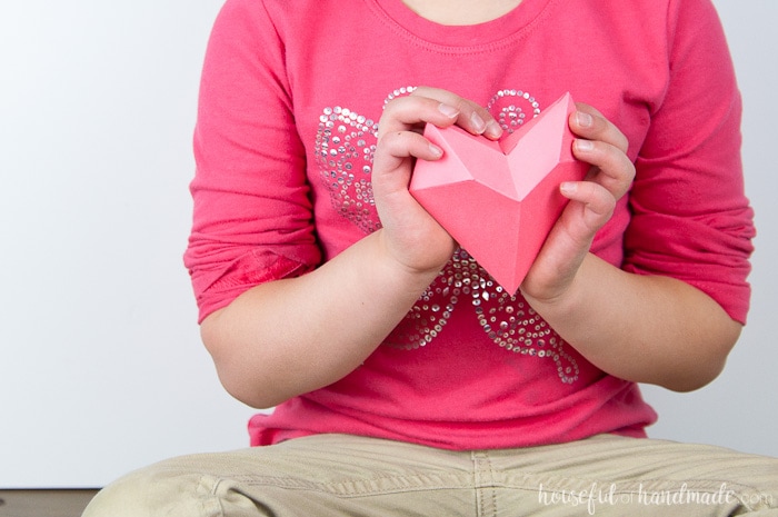 3D paper heart being held up against the chest where the heart is by a child. 