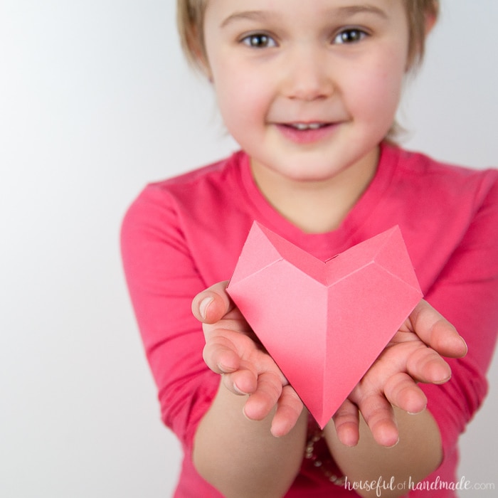 Little girl holding a 3D paper heart made out of pink cardstock in her hands. 