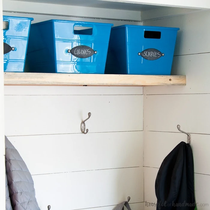 Blue dollar store bins in the mudroom with chalkboard labels on the front to keep things organized. 