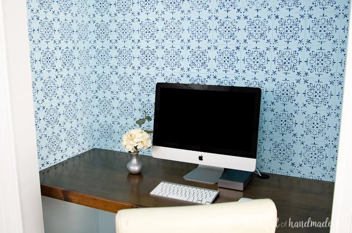 office in closet shown with finished blue patterned wall paper, wood desk top and computer