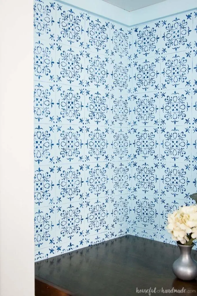 inside of office closet with wood desk and blue wall paper with vase of white flowers