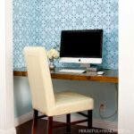Office in closet shown with wood desk, office chair, blue wall paper and iMac computer.