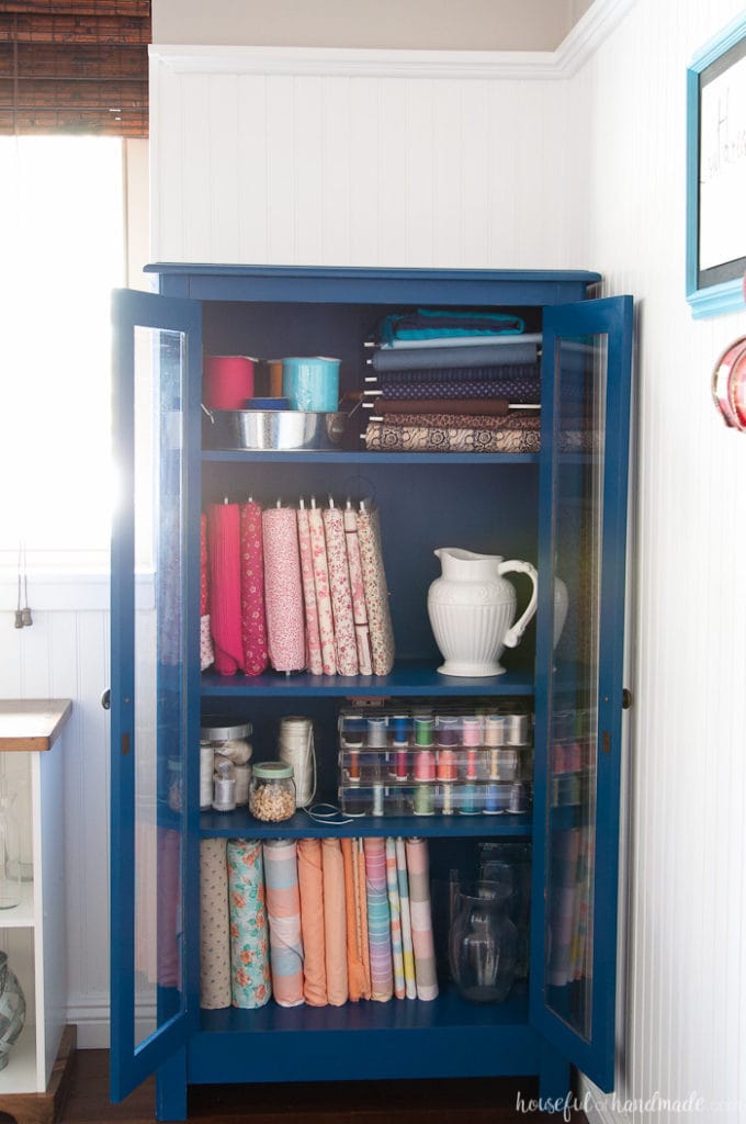 Cabinet in craft room with fabrics and sewing supple organized in it. 