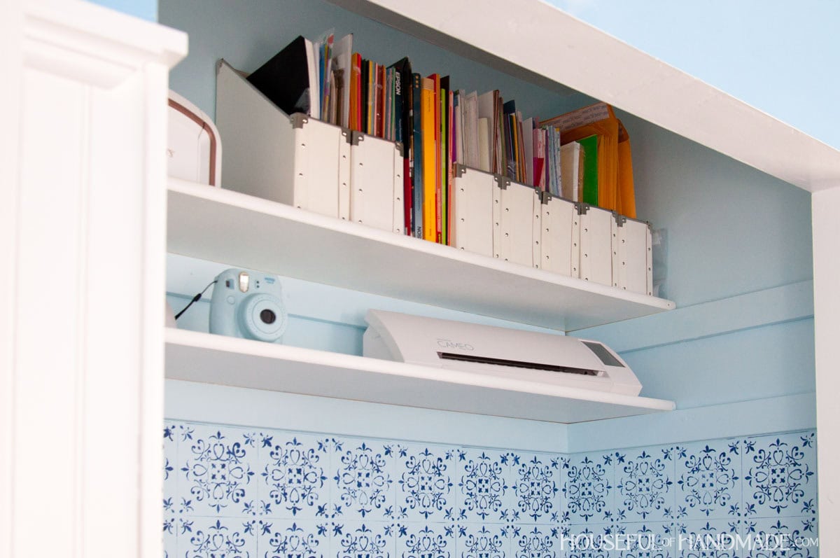 Storage shelves in office closet with blue painted walls with stencil.