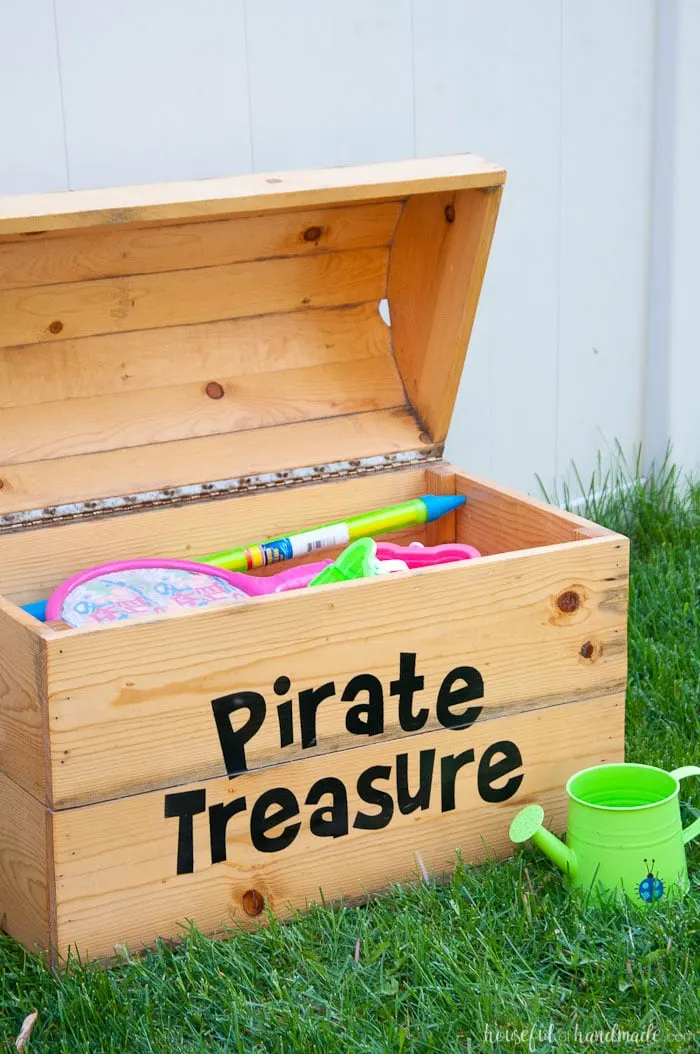 DIY treasure chest toy box shown outside with open lid and filled with kids toys.