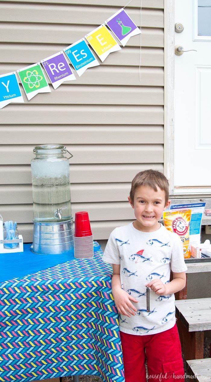 young boy smiling at his science themed birthday party with banner in the back ground.