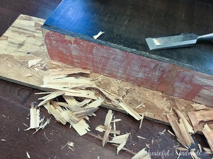 Toe kick being shaved smaller with a chisel and lots of chips of wood on the floor next to it. 