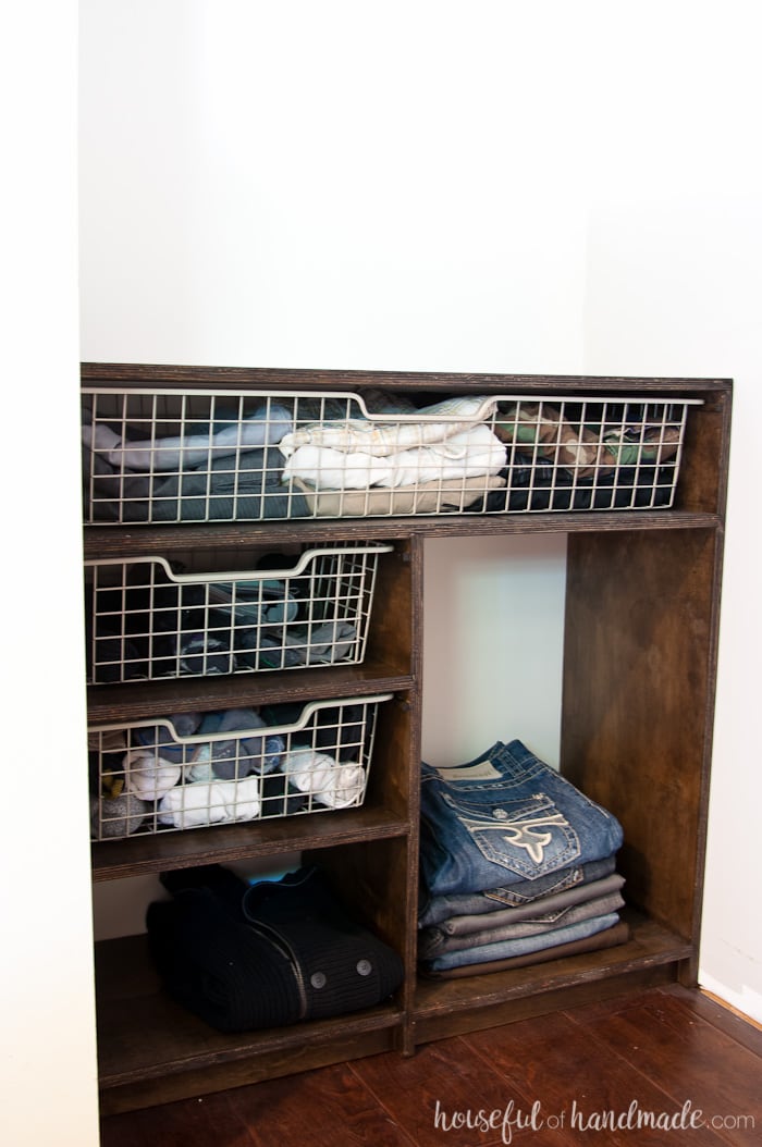 Other side of the DIY closet organizer with Ikea baskets in the cubbies and pants stacked in a shelf.