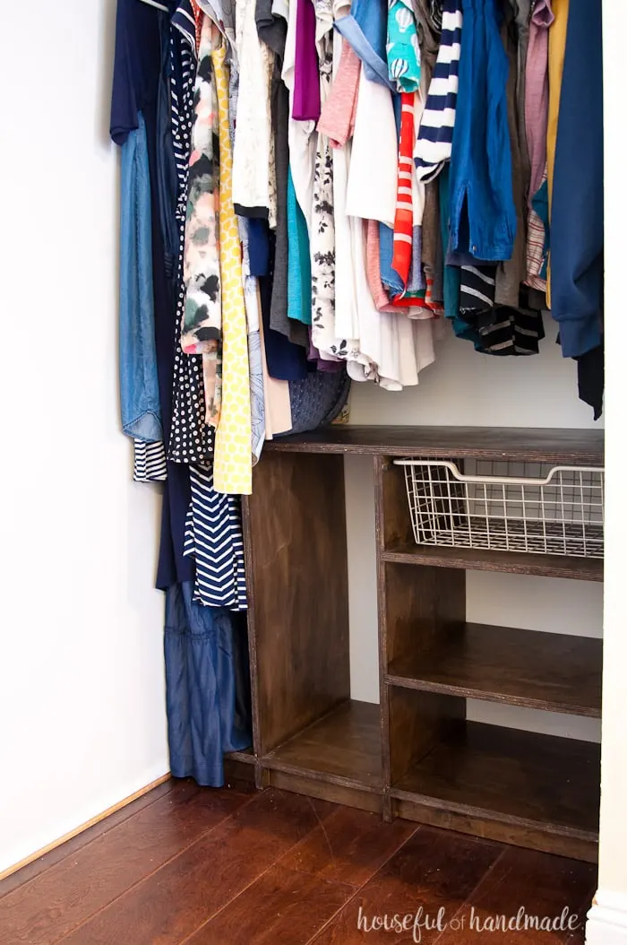 Custom closet system made from plywood and stained walnut on one side of the closet with clothes hanging above and to the side of it.