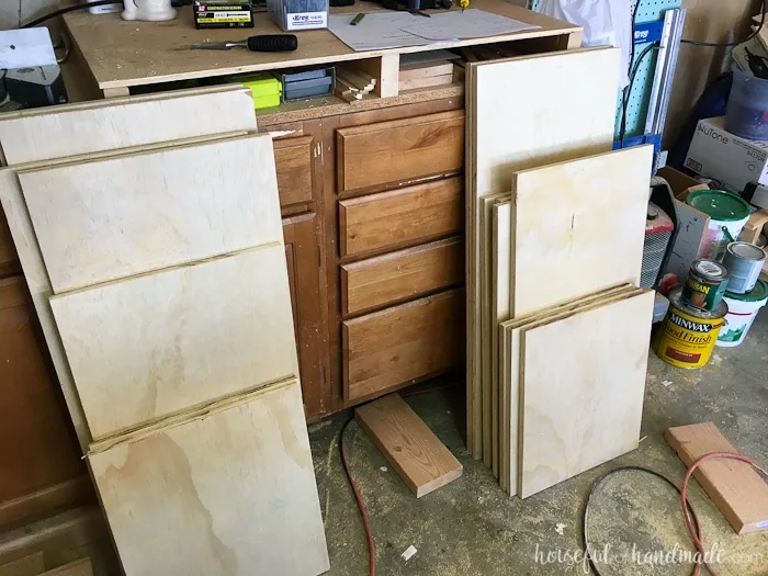 All the cut plywood pieces stacked up against the workbench in a garage. 