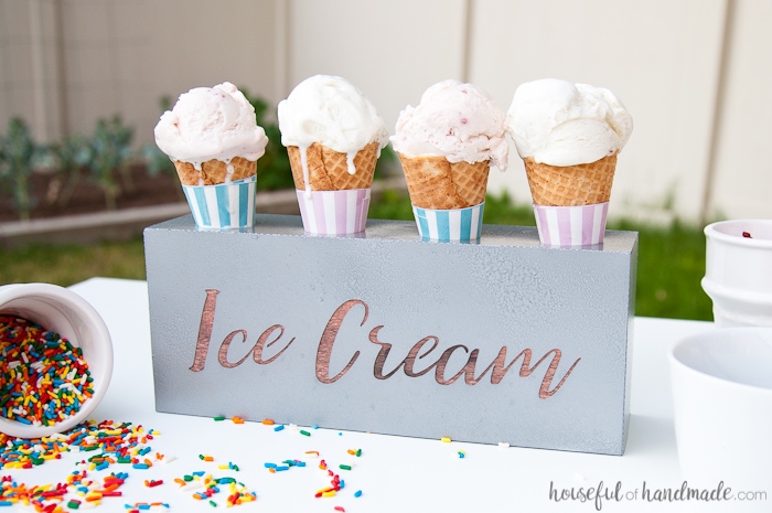 DIY farmhouse ice cream cone holder on an outdoor table.  Sprinkles container on its side with two other white containers