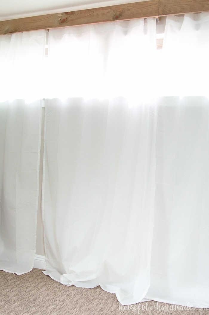 Wall with short windows high on the wall covered by white sheer curtains and a rustic DIY valance.