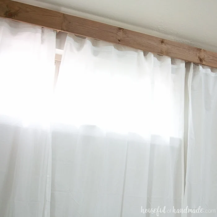 Wall of white curtains with a wood stained cornice box over the curtain rod. 