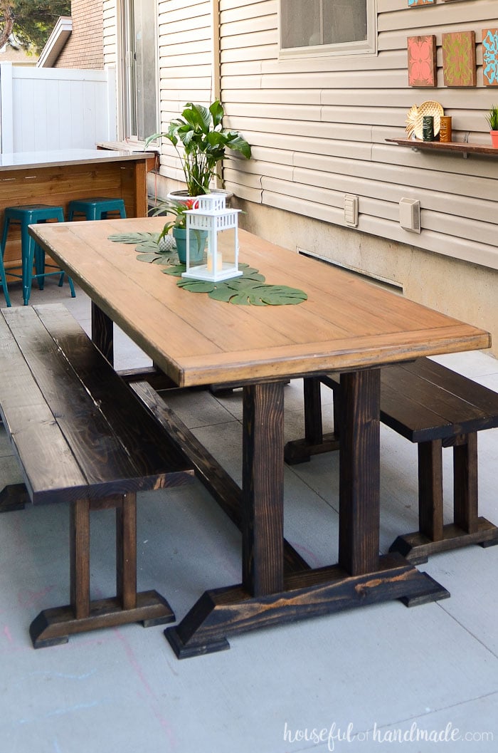 Outdoor dining table with dark stained benches on a patio.