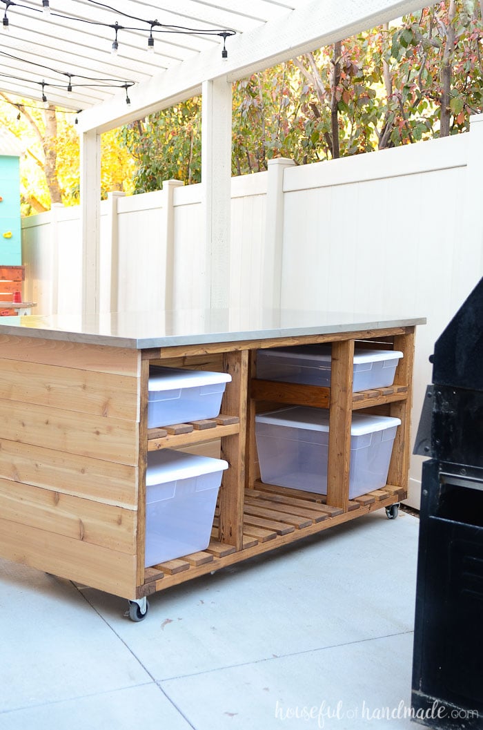 White painted pergola with rolling kitchen island filled with storage bins. 