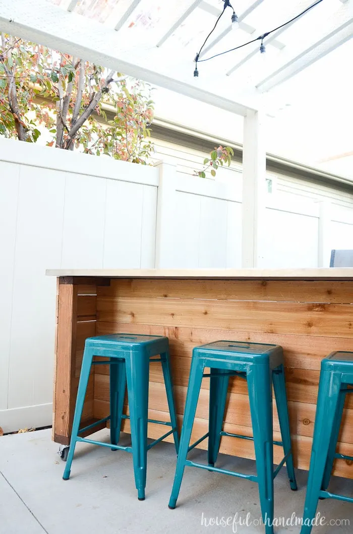 Counter height seating area on the back of an outdoor table with turquoise metal stools. 