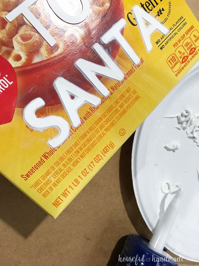 caulk shown being added to the letters to help them appear like punched metal on empty cereal box