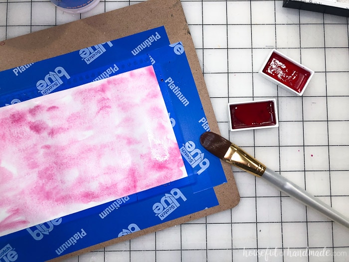 Piece of paper taped to a clip board with pink watercolor paint on it. Used to decorate a large glass candle holder. Housefulofhandmade.com