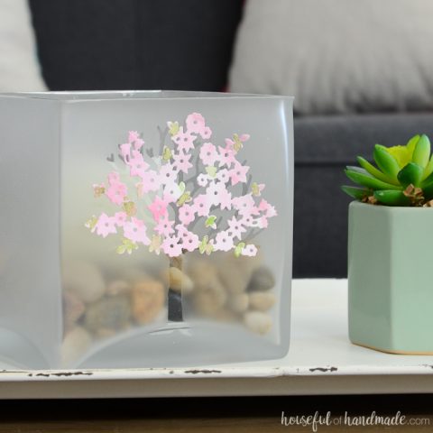 Large glass candle holder decorated with a frosted tree and spring blossoms on a tray in a living room. Housefulofhandmade.com