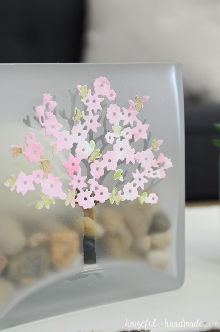 Frosted glass jar with etched tree design and watercolor spring blossoms filled with rocks and a candle. Housefulofhandmade.com