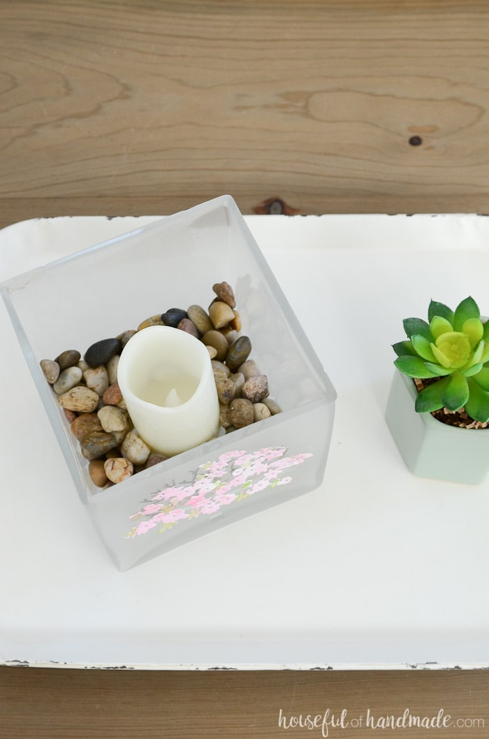 A square candle holder filled with rocks and a candle on a white tray. Housefulofhandmade.com