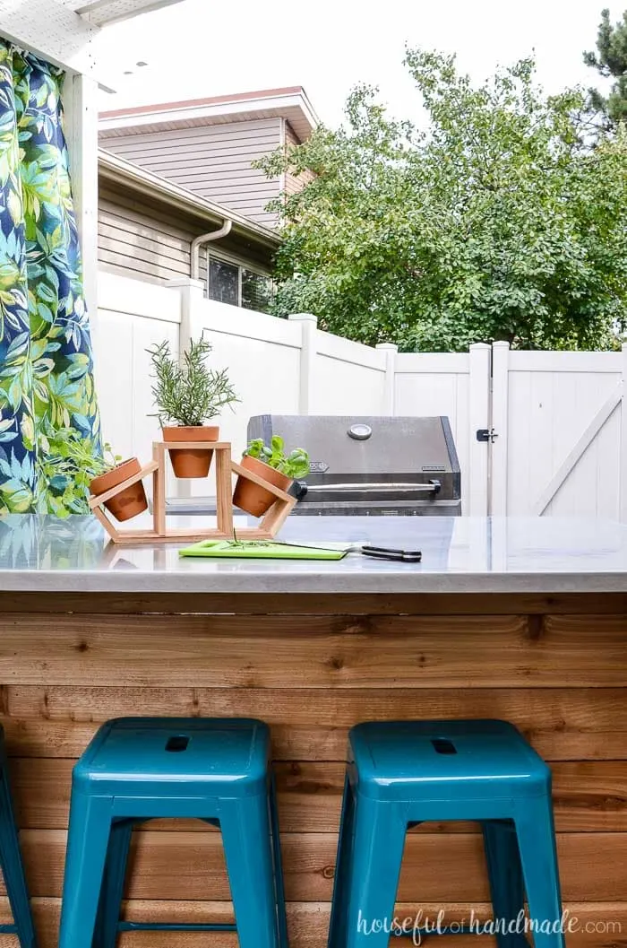 Outdoor kitchen island in front of a BBQ. Cedar countertop herb garden on top of the outdoor kitchen table. Housefulofhandmade.com