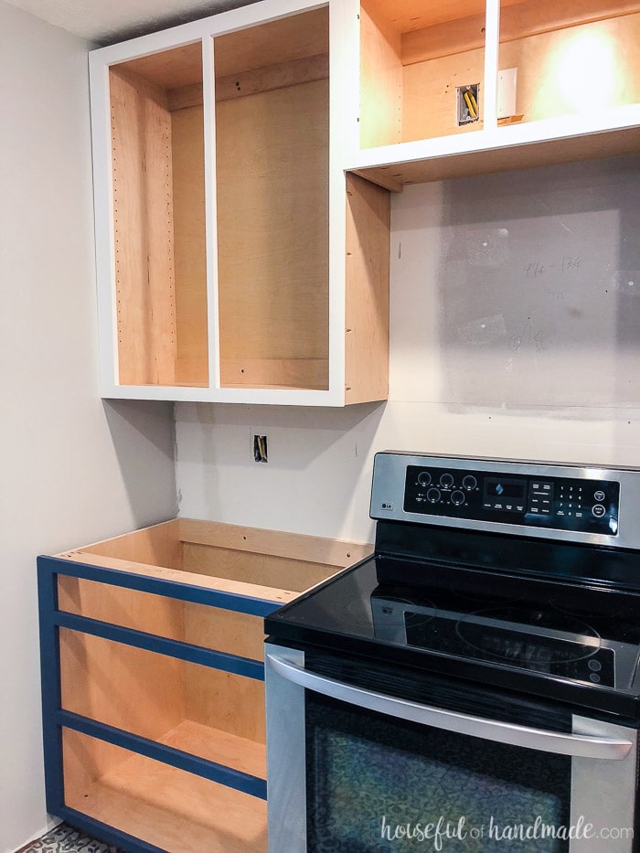 Kitchen with cabinets installed without cabinet doors yet. Base cabinet is a drawer base and uppers are over stove.