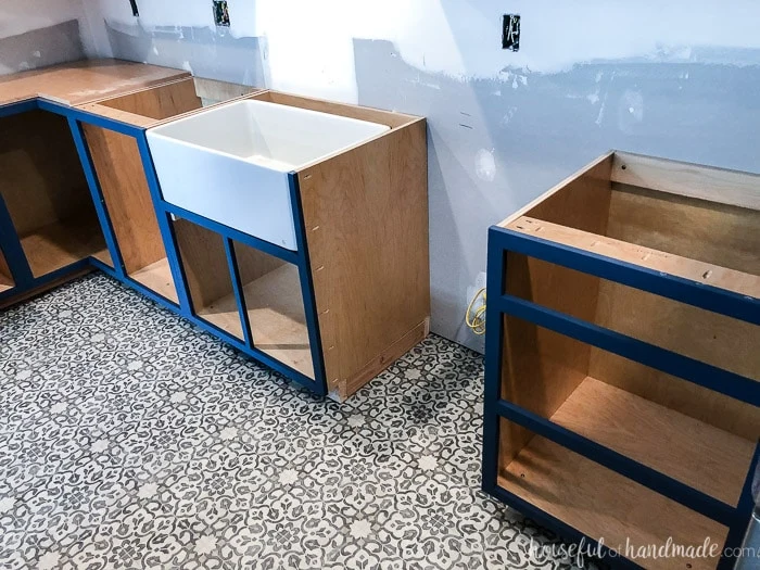 Navy blue face frame DIY base cabinets installed in a kitchen without their doors yet, including a custom apron front sink base cabinet.
