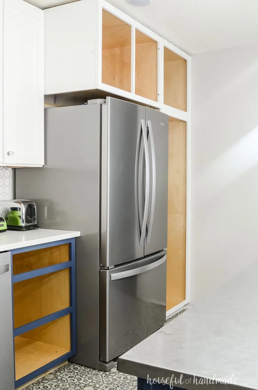 Stainless steel refrigerator surrounded by deep pantry cabinets painted white.