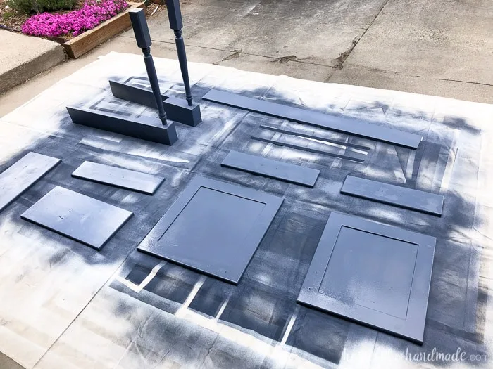 Wood pieces for kitchen island shown outside on tarp being painted with paint sprayer.