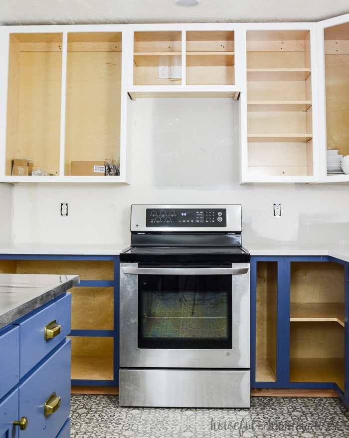 White painted upper cabinets with soft navy base cabinets missing their doors. See how to paint unfinished cabinets at Housefulofhandmade.com.