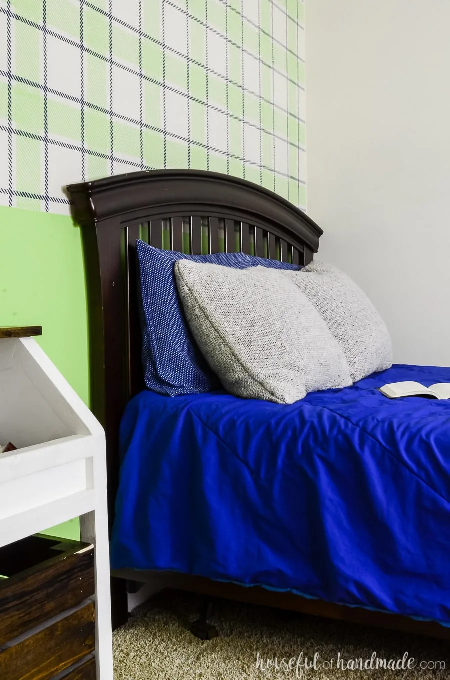 Dark wood craftsman headboard in a boys bedroom. Blue bedding with a green plaid wall design on the back wall.