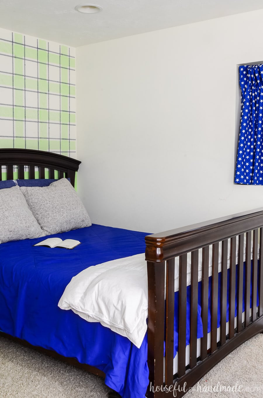 Dark wood bed with blue comforter and knit pillows. Focal wall behind bed is painted blue & green plaid with a wall stencil. 