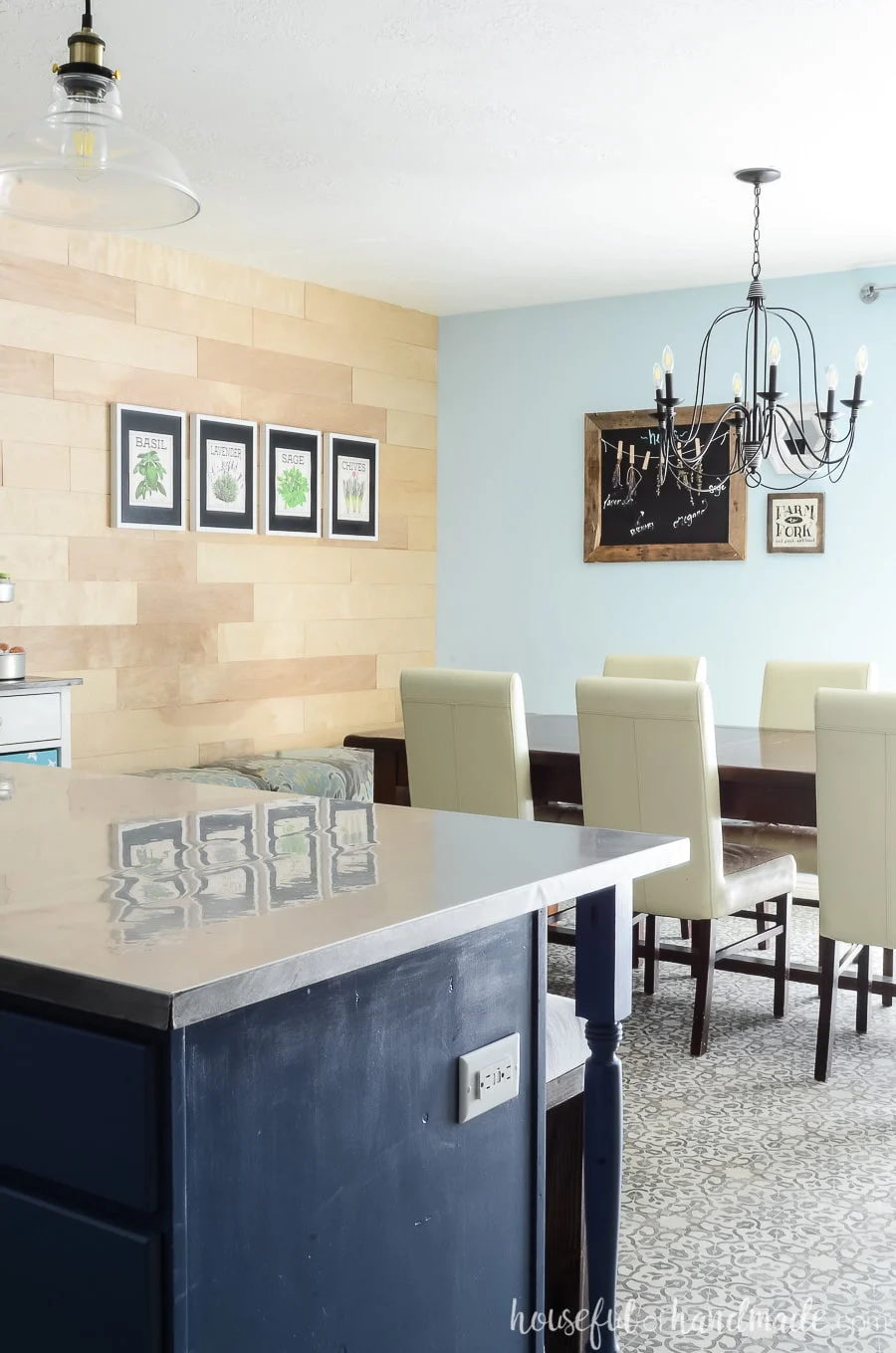 Navy blue kitchen island with stainless steel countertop looking out over dining room with farmhouse table and wood accent wall.