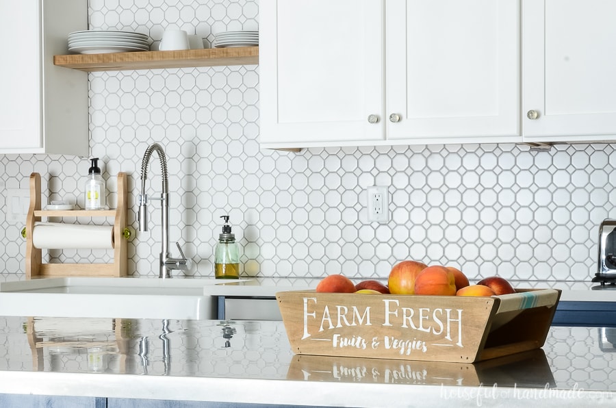 Farmhouse fruit bowl on kitchen island in front of white kitchen cabinets with white porcelain backspace. 